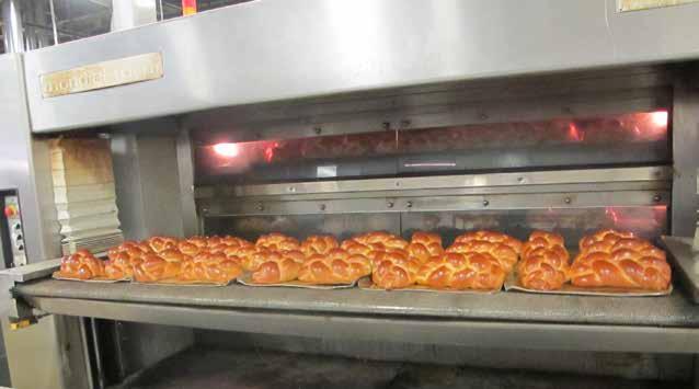 Freshly baked loaves of challah bread leave the three-deck tunnel oven, then are racked and cooled before packaging. before customers open at the break of dawn.