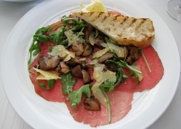 Beef Carpaccio Beef carpaccio is a dish typically consisting of thin slices of raw or partially cooked beef, served with arugula, parmesan cheese and dressing.