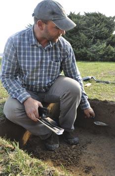 Jason Shellenhamer, field supervisor for the Louis Berger Group, points out differences in soil strata visible in an excavated sample pit during an archeological survey conducted in April 2013 on NSF