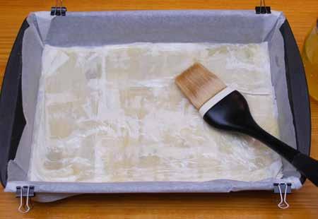 7 5 Begin by placing a sheet of phyllo dough in the bottom of the pan, lengthwise end to end. It might be slightly larger. Brush carefully with melted butter. It will tear easily at this point.