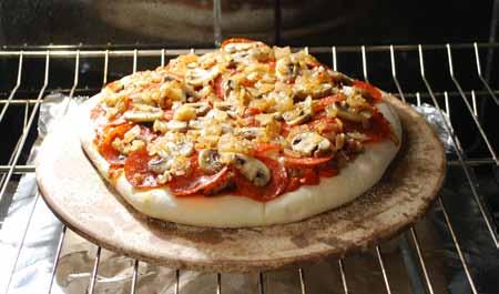 I also sprinkle it with some oregano flakes. 15 Here is my pizza, baking on the pizza stone in the oven. I put a sheet of foil on the rack underneath to catch any corn meal that might fall off.