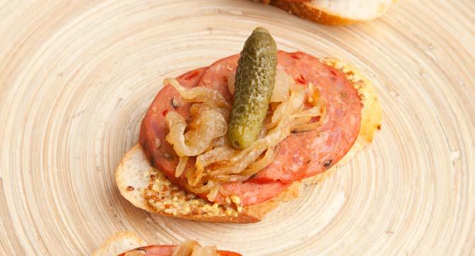 Spicy Italian Style Salami Crostini SERVES 8 1/2 Spicy Italian Style Salami, sliced thin 3 Tbs. whole grain mustard 16 slices baguette, cut on a bias, ¼1/4 thick. 3 Tbs. caramelized onions 16 Cornichons (small French pickles) 1.