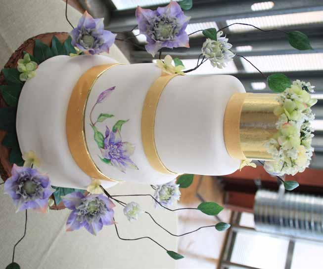 Cali Chic White fondant with hand painted clematis and coordinated floral embellishments. Gold topper and bands add elegance to this otherwise natural design.