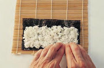Wetting your hands with cold water to keep the rice from sticking to them, spread a layer of sushi rice over the