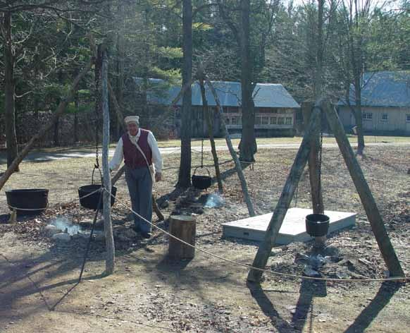 A costumed interpreter checks the iron cauldrons of sap hung from large tripods in Westfield Heritage Village.