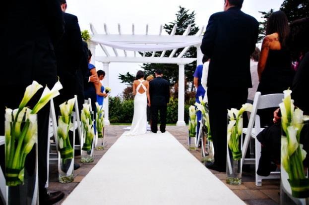 Creating your Wedding Experience, Oceano Hotel Event Space WEDDING GARDEN Behind a gated white fence and ornamental bushes is a stone walkway lined with decorative shepherd hooks.
